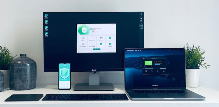 Desk setup displaying kaspersky cybersecurity software running on a Dell monitor, MacBook, and smartphone, illustrating cross-device protection and digital security