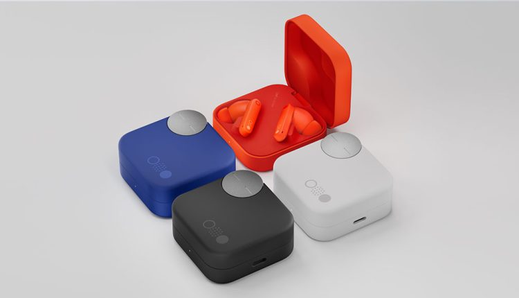 A collection of CMF Buds Pro 2 earbuds and their charging cases, displayed on a light grey surface. One orange case is open, revealing bright orange earbuds. Three other cases are closed: one in royal blue, one in black, and one in white. Each closed case has a prominent circular silver dial on top.