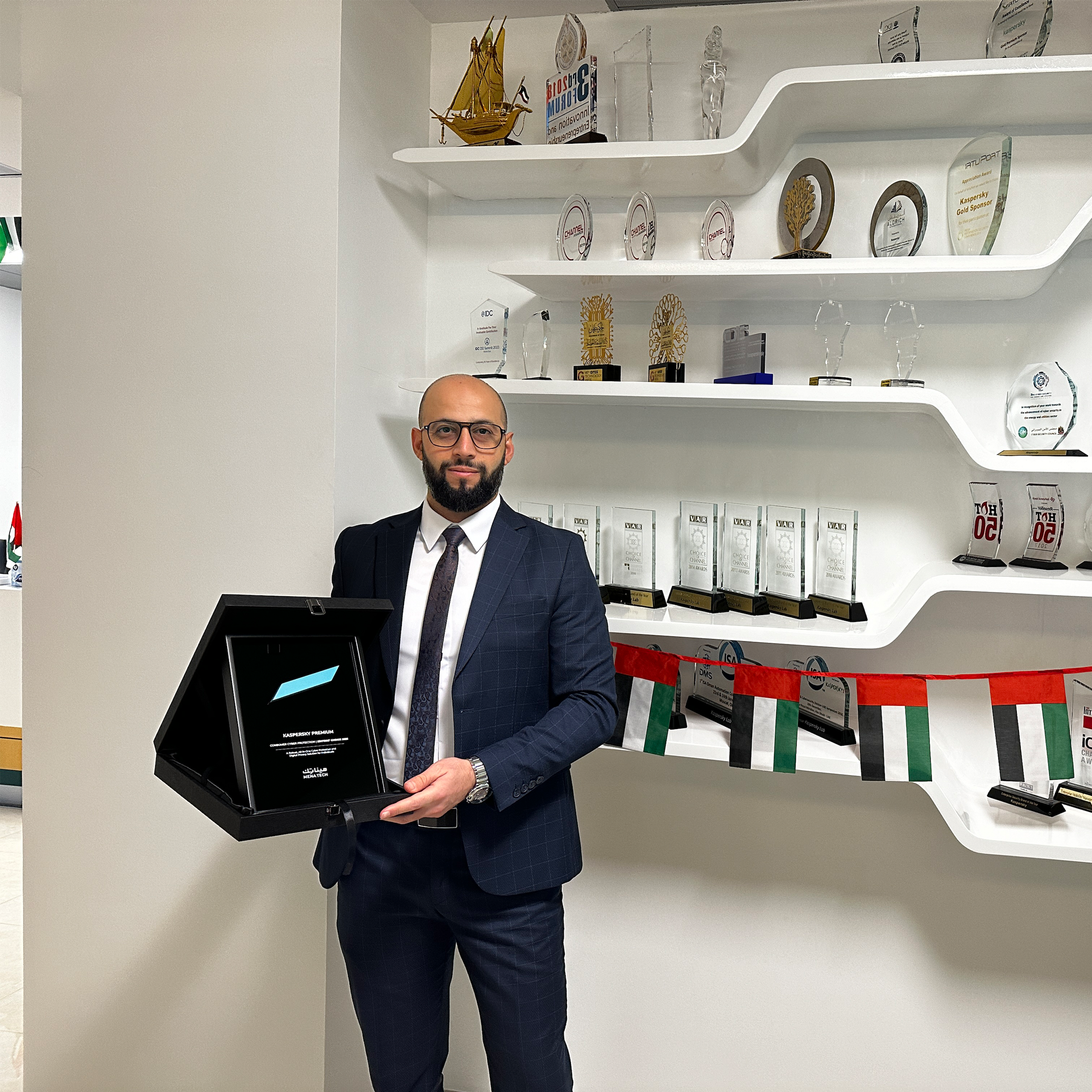 A Kaspersky representative holding the MENA Tech Editors' Choice 2025 award for Kaspersky Premium, standing in front of a display shelf with trophies and UAE flags