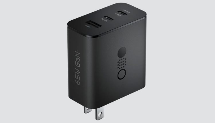 A black CMF by Nothing 65W GaN charger with a US plug, angled slightly to reveal its side and top. The side has "65W GaN" lit up in white dots, and a circular button with speaker-like perforations. The top features multiple USB-C and USB-A ports.